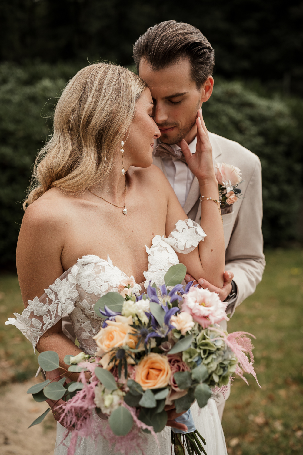 Braut ist an Bräutigam geschmiegt, Brautstrauß ist im Vordergrund